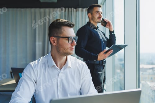 Preview: Two male focused colleagues discussing business project looking at laptop screen