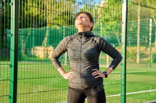 Preview: Active sporty mature woman standing in sports stadium, after training, running, exercising