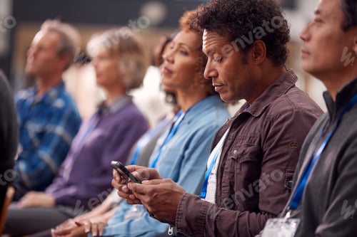 Preview: Businessman In Presentation At Conference Checking Mobile Phone