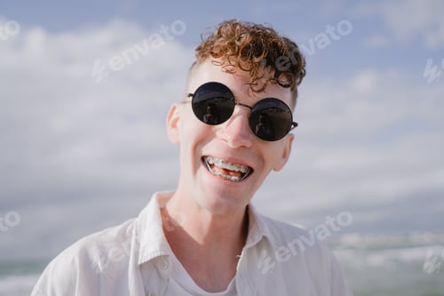 Preview: young guy smiling with braces on his teeth, with curly hair and sunglasses
