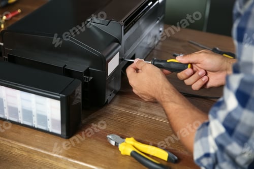 Preview: Repairman with screwdriver fixing modern printer indoors, closeup