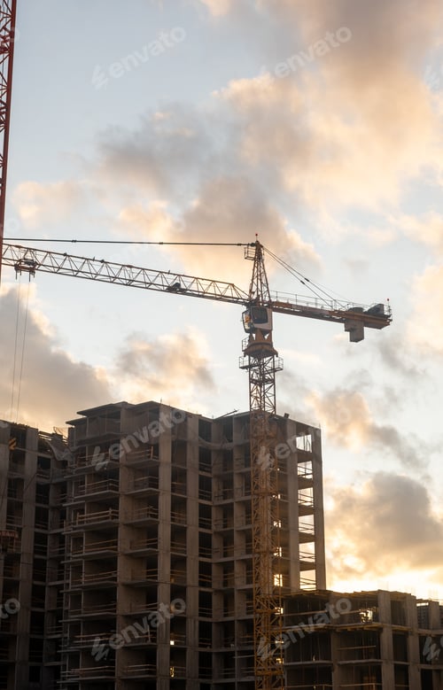 Preview: Cranes are positioned at a construction site, silhouetted against a colorful sunset with clouds