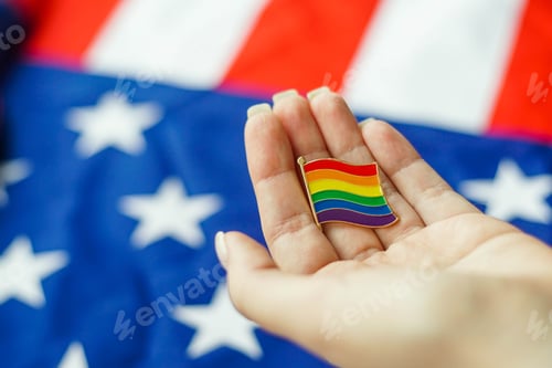 Preview: Close up of young woman holding LGBT icon in her hand. American flag on the background. Close up.