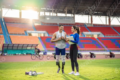 Preview: Asian athlete with prosthetic blades and trainer workout in stadium.