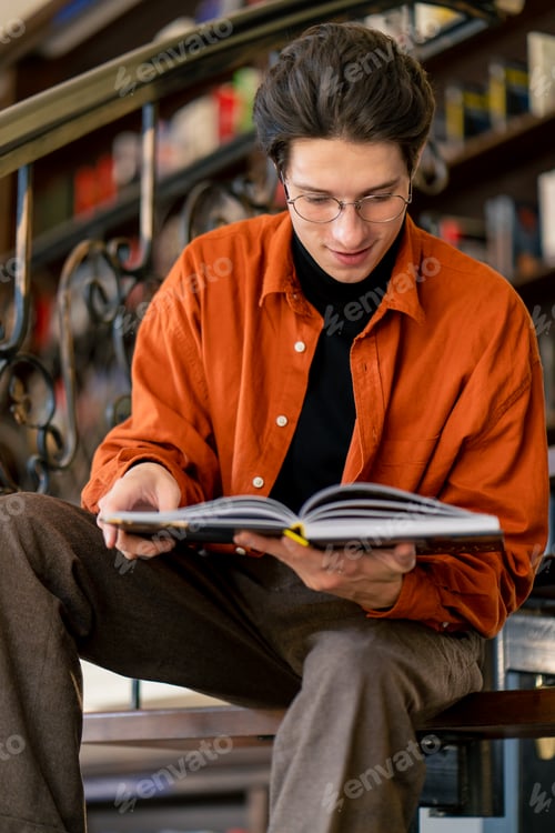 Preview: a young guy in glasses sits on the stairs carefully reads a book manual prepares for exams