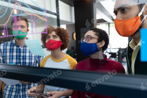 Preview: Diverse group of colleagues wearing face masks brainstorming at glass wall in office
