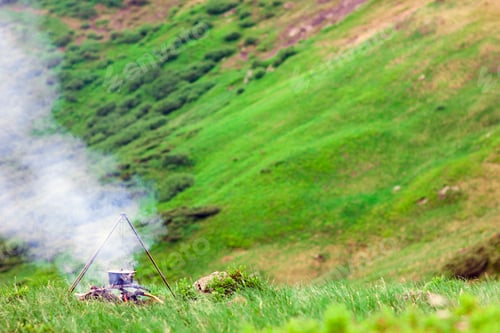 Preview: Camping fire and tourists bowler with preparing food in mountains