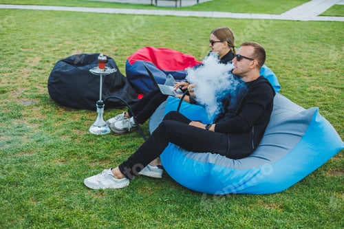 Preview: A young couple relaxes in the park and smokes hookah. A man and a woman sit on chairs in nature