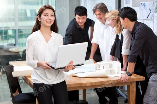 Preview: Architect holding laptop in studio with her team in background
