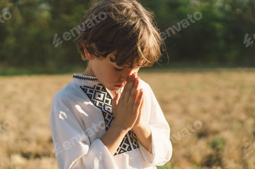 Preview: A young child wearing a traditional embroidered shirt quietly prays outdoors