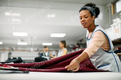 Preview: African American seamstress using fabric roll while working at textile factory.