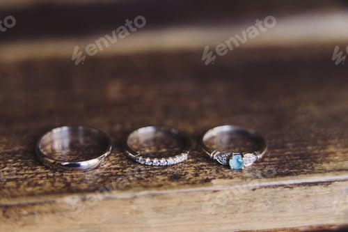 Preview: Wedding rings with diamonds and engagement ring with blue gemstone on wooden background.