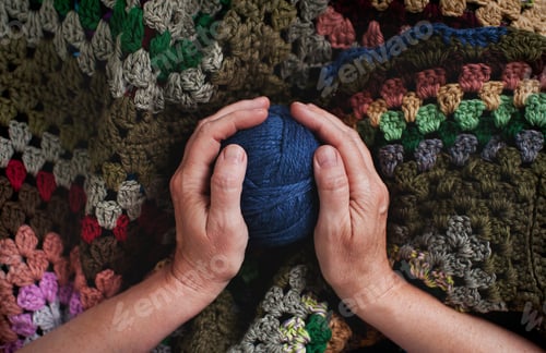 Preview: Hands Holding Blue Yarn with Colorful Crochet Blanket