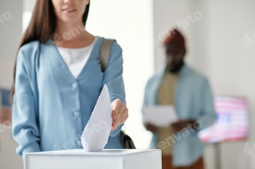 Preview: Focus on hand of young female voter putting ballot paper into box