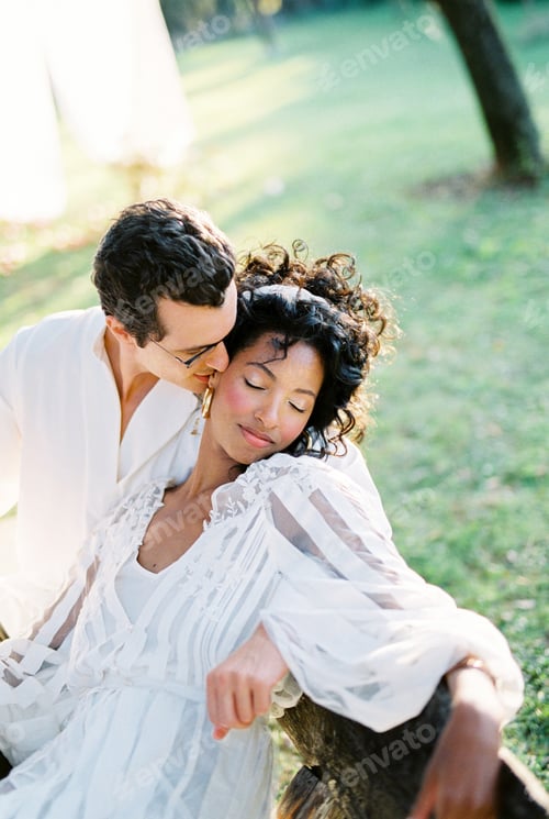 Preview: Man hugs and kisses a woman sitting on a bench
