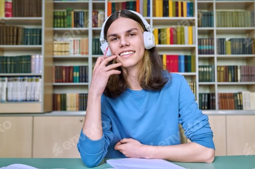 Preview: Teenage college student in headphones looking at webcam, sitting at desk in library