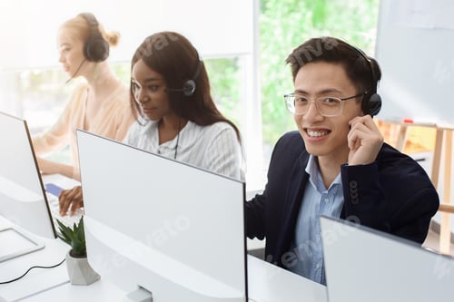 Preview: Customer support phone operators in headsets behind computer monitors at call center, empty space