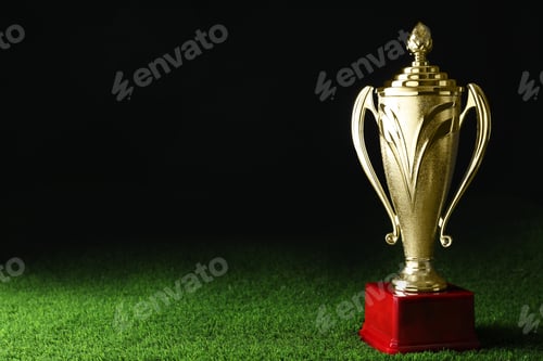 Preview: Golden trophy cup on green grass against black background. Space for text