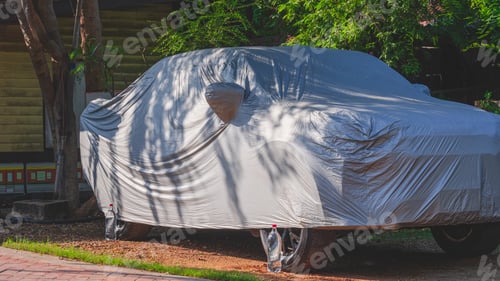 Preview: A car under protective cover cloth parked under the shade of tree outside of house