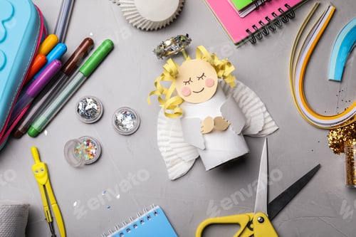 Preview: Toy angel made of toilet paper hub among stationery on grey table, flat lay