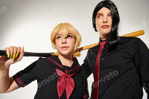 Preview: couple of cosplayers in wigs and school uniform with baseball bats looking away on grey, subculture