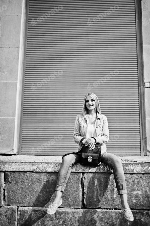 Preview: Blonde girl wear on jeans jacket with backpack posed against orange shutter.