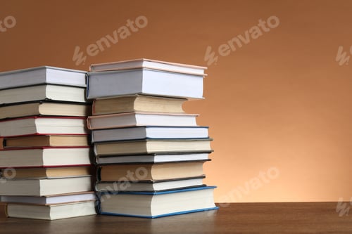 Preview: Stacks of many books on wooden table against light brown background, space for text
