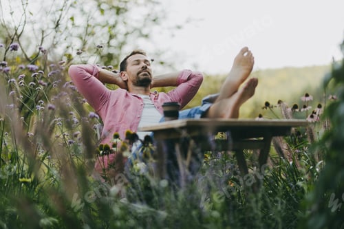 Preview: Relaxed man sitting in the garden with feet on table. Father having moment to himself while his kids