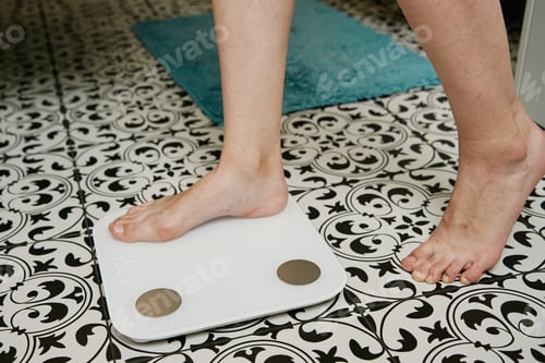 Preview: Woman checking her weight on weighing scales in bathroom