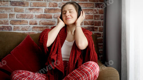 Preview: Happy cheerful woman listening music and dancing on sofa in living room