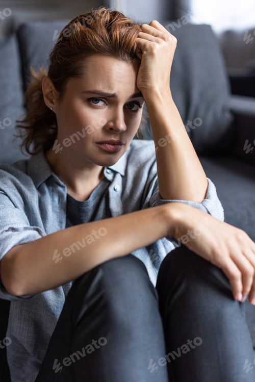 Preview: selective focus of upset woman looking at camera while sitting at home
