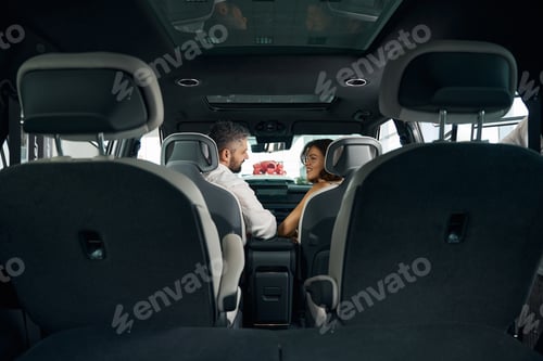 Preview: Loving couple looking each other sitting in new car in auto showroom
