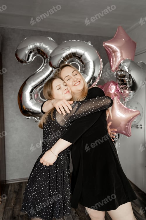 Preview: two girls hugging and with a happy smile on their faces, on the background of balloons