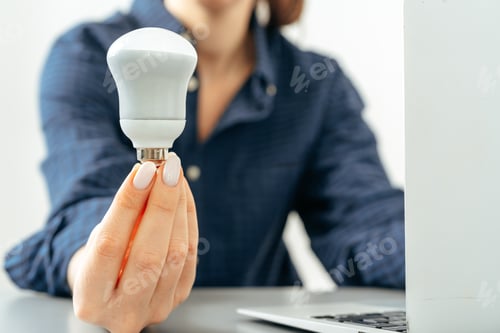 Preview: Female hand holding a light bulb above the table