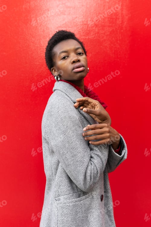 Preview: Side view of emotionless African American woman with short hair in warm jacket and earrings looking