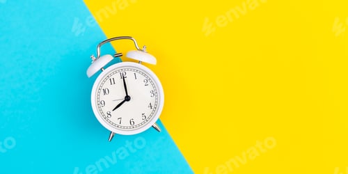 Preview: White alarm clock on a blue and yellow background, flat lay.