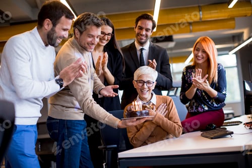 Preview: Young colleagues celebrate an older colleague's birthday at the office and bring a cake