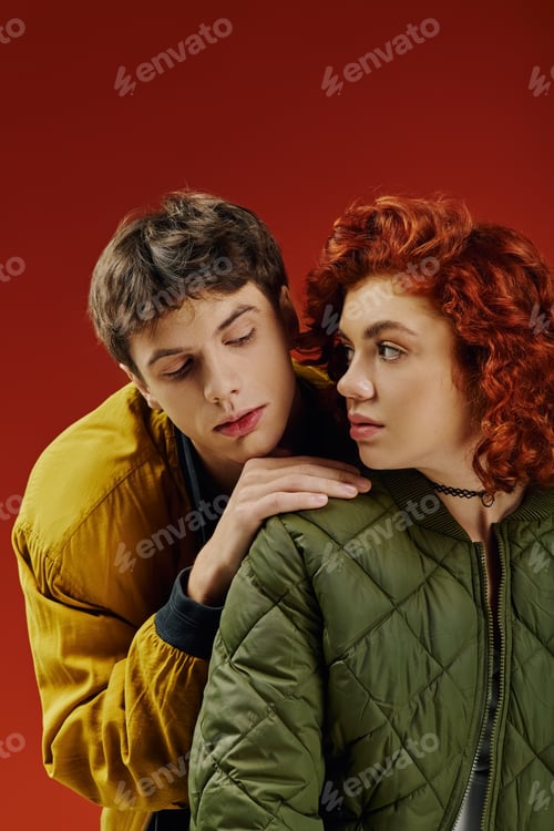 Preview: stylish appealing couple in fashionable vibrant clothing posing together on red background