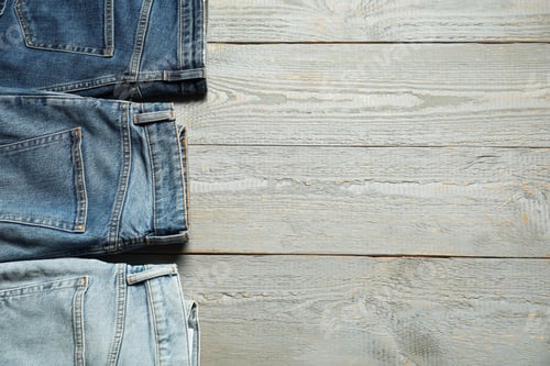 Preview: Different stylish jeans on grey wooden background, flat lay. Space for text