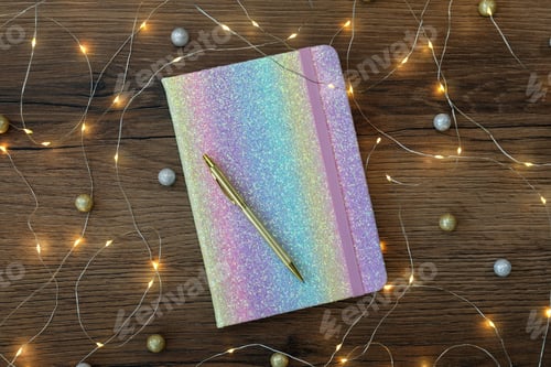 Preview: Stylish planner, pen and Christmas lights on wooden background, flat lay. New Year aims