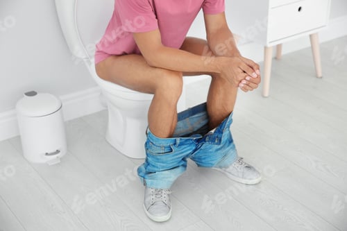 Preview: Young man sitting on toilet bowl at home
