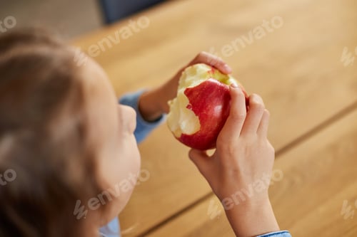 Preview: Cute little girl eat red apple at home at kitchen interior