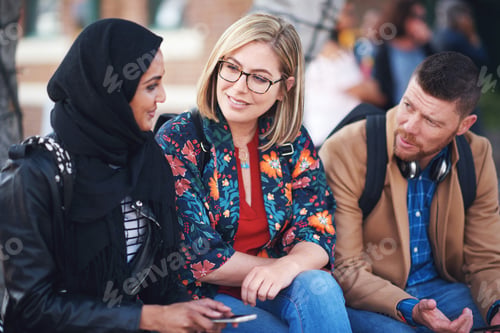 Preview: Multiracial friends hanging out sitting on bench in city chatting
