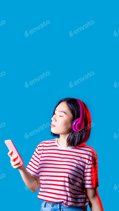 Preview: Young asiatic woman isolated listening music holding smartphone