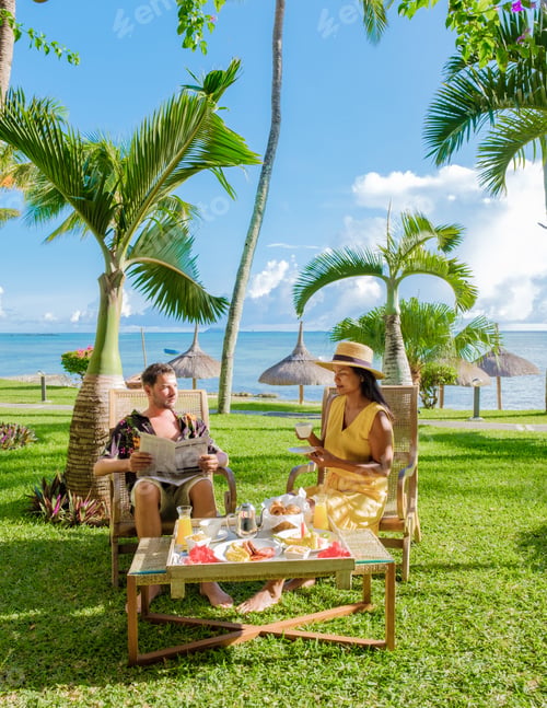 Preview: Man and Woman having breakfast in a garden with palm trees on a tropical beach in Mauritius