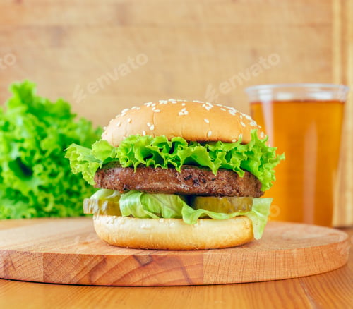 Preview: Freshly made burger with lettuce and pickles served with a refreshing drink on a wooden table