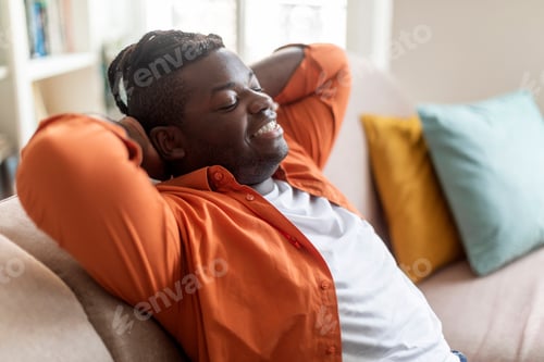 Preview: Happy african american man reclining on sofa at home