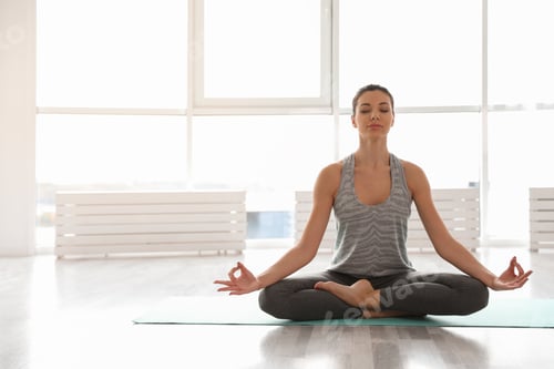 Preview: Young woman practicing yoga in studio. Accomplished pose (Siddhasana)