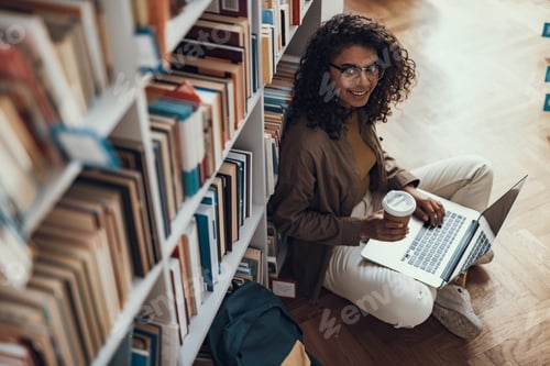 Preview: Smiling Pretty Student Feeling Good And Smiling While Sitting Against The Bookcase On The Floor