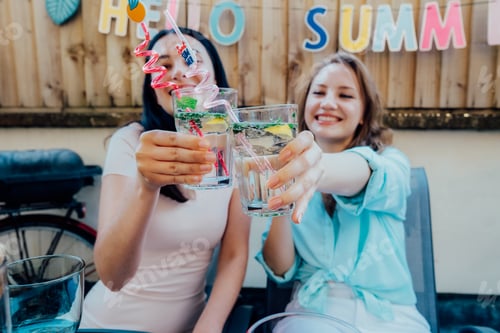 Preview: Focus on glasses with cocktails in female hands enjoying summer party on outdoor terrace with drinks